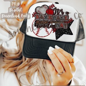 May include: White trucker hat with a black mesh back. The front of the hat features a baseball-themed design with a red heart, baseballs, a bat, and the text "It's a Baseball kinda day".