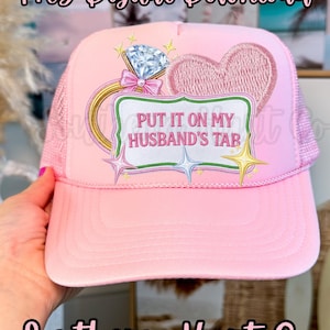 Pode incluir: Boné rosa estilo trucker com parte traseira em rede e aba curva. O boné apresenta um design bordado de um anel de diamante, um coração e o texto "PUT IT ON MY HUSBAND'S TAB". As palavras "PNG Digital Download" e "Southern Hart Co" também são visíveis.