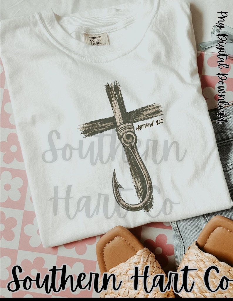 K&ouml;nnte beinhalten: Ein wei&szlig;es kurz&auml;rmeliges T-Shirt mit einer Grafik eines dunkelbraunen Kreuzes, das mit einem Angelhaken verschlungen ist. Der Text Matthew 4:19 ist neben dem Kreuz aufgedruckt. Das T-Shirt hat ein Comfort Colors Etikett am Innenkragen.