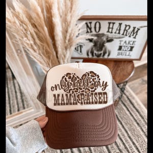 Op de afbeelding: Bruine en witte truckercap met een luipaardprint hart en de tekst "only hell my mama raised".