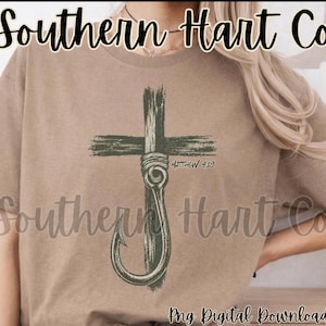 K&ouml;nnte beinhalten: Ein beiges Kurzarm-T-Shirt mit einer dunkelgr&uuml;nen Grafik eines Holzkreuzes, das mit einem gro&szlig;en Angelhaken verschlungen ist. Der Text Matthew 4:19 ist in einer kleinen, dunklen Schrift neben dem Haken gedruckt. Das Design hat eine abgenutzte Optik.