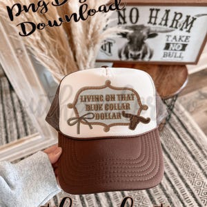 Può includere: Cappellino da camionista marrone e bianco con la scritta "Living on that Blue Collar Dollar" e una grafica a forma di testa di toro. Il cappellino ha una visiera marrone e un retro in rete, con le parole "No Harm Take No Bull" sullo sfondo.