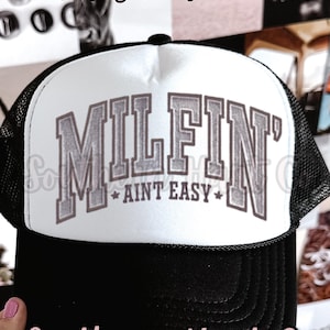 Puede incluir: Gorra de camionero en blanco y negro con el texto "MILFIN' AINT EASY" en letras grises. La gorra tiene un panel frontal blanco y una parte trasera de malla negra. También se ven las palabras "PNG Digital Download" y "Southern Hart Co".