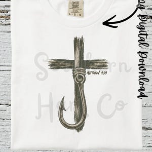 K&ouml;nnte beinhalten: Ein wei&szlig;es T-Shirt mit einer Grafik eines dunkelbraunen Holzkreuzes, das mit einem Angelhaken und einem Seil umwickelt ist. Der Text 'Matthew 4:19' ist in Schwarz neben dem Haken aufgedruckt. Das T-Shirt hat ein Comfort Colors Markenetikett am Kragen.