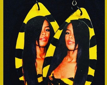 May include: A pair of yellow and black striped wooden earrings with a photo of a woman on each earring.
