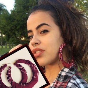 Op de afbeelding: Grote bordeauxrode stoffen oorringen met een wit paisley patroon. De oorbellen zijn cirkelvormig, met een goudkleurige metalen pin. De stof is om de ringen gewikkeld. De oorbellen worden in een vierkant frame getoond.
