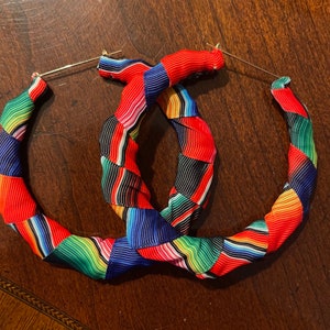 May include: A pair of large hoop earrings with a colorful striped pattern. The stripes are red, green, blue, black, and white.