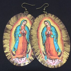 May include: A pair of oval-shaped earrings with a gold background and a colorful image of the Virgin Mary. The earrings have a brown wooden frame and gold accents.