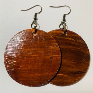 May include: A pair of brown wooden circle earrings with gold-toned hooks. The earrings have a wood grain pattern and a glossy finish.