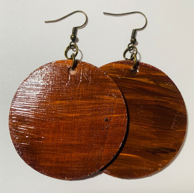 May include: A pair of brown wooden circle earrings with gold-toned hooks. The earrings have a wood grain pattern and a glossy finish.