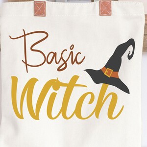 May include: A white canvas tote bag with brown straps and the text "Basic Witch" in brown and yellow lettering. A black witch hat with a brown buckle is next to the text.