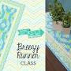 May include: A blue and green table runner with a wavy pattern. The runner is on a table with a potted plant. The text "Breezy Runner Class" is visible in the image.