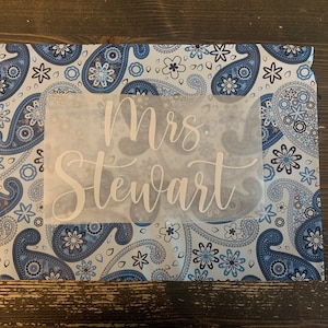 May include: A white fabric sheet with the text "Mrs. Stewart" printed in a cursive font on a blue and white paisley patterned fabric background.
