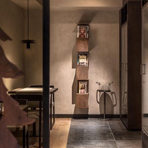 May include: A modern interior design with a brown wooden tree sculpture, a dark wood table with chairs, and a wall-mounted shelf with magazines. The shelf is made of metal and has a rustic look.