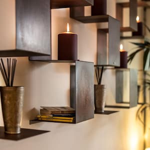 May include: A set of brown metal shelves with a variety of items on them, including candles, books, and decorative objects. The shelves are mounted on a white wall.