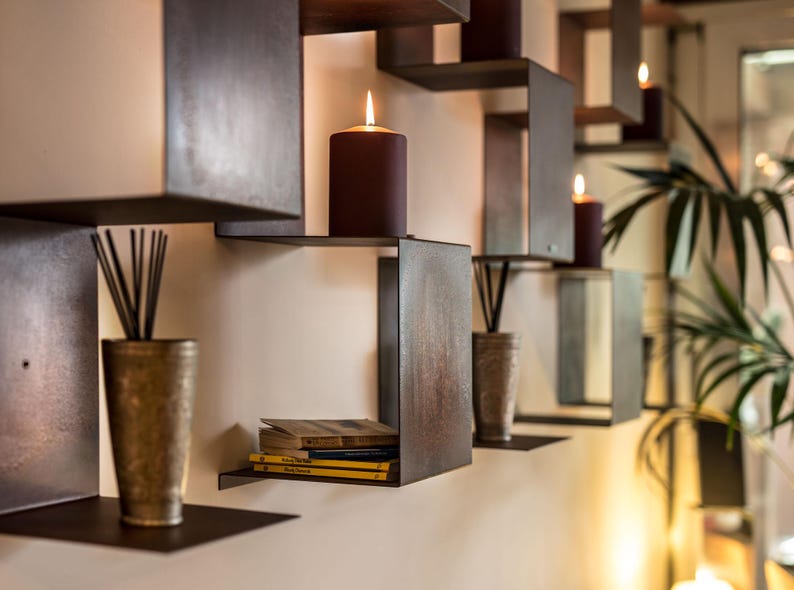 May include: A set of brown metal shelves with a variety of items on them, including candles, books, and decorative objects. The shelves are mounted on a white wall.