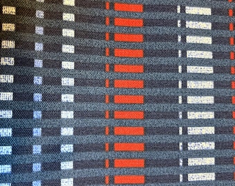May include: A woven fabric featuring a repeating geometric pattern of vertical stripes in dark blue, bright orange, and white. The texture shows a grid-like weave with alternating blocks of color that create a structured, linear design across the surface.