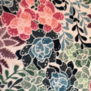 May include: A soft, textured fabric featuring a dense, repeating pattern of succulents and floral shapes in shades of pink, deep red, dark blue, light blue, sage green, and dark forest green, all set against a creamy off-white background.