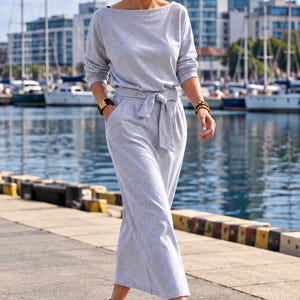 Puede incluir: Un vestido midi de color gris claro con mangas largas, escote barco y un cinturón de tela a juego en la cintura. El vestido cuenta con bolsillos laterales y se combina con zapatillas de lona blancas de corte bajo con cordones blancos.