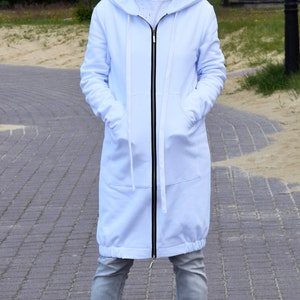 May include: A long, light blue hooded sweatshirt with a zipper closure. The sweatshirt has a relaxed fit and a drawstring hood. The model is wearing the sweatshirt with grey jeans and white sneakers.