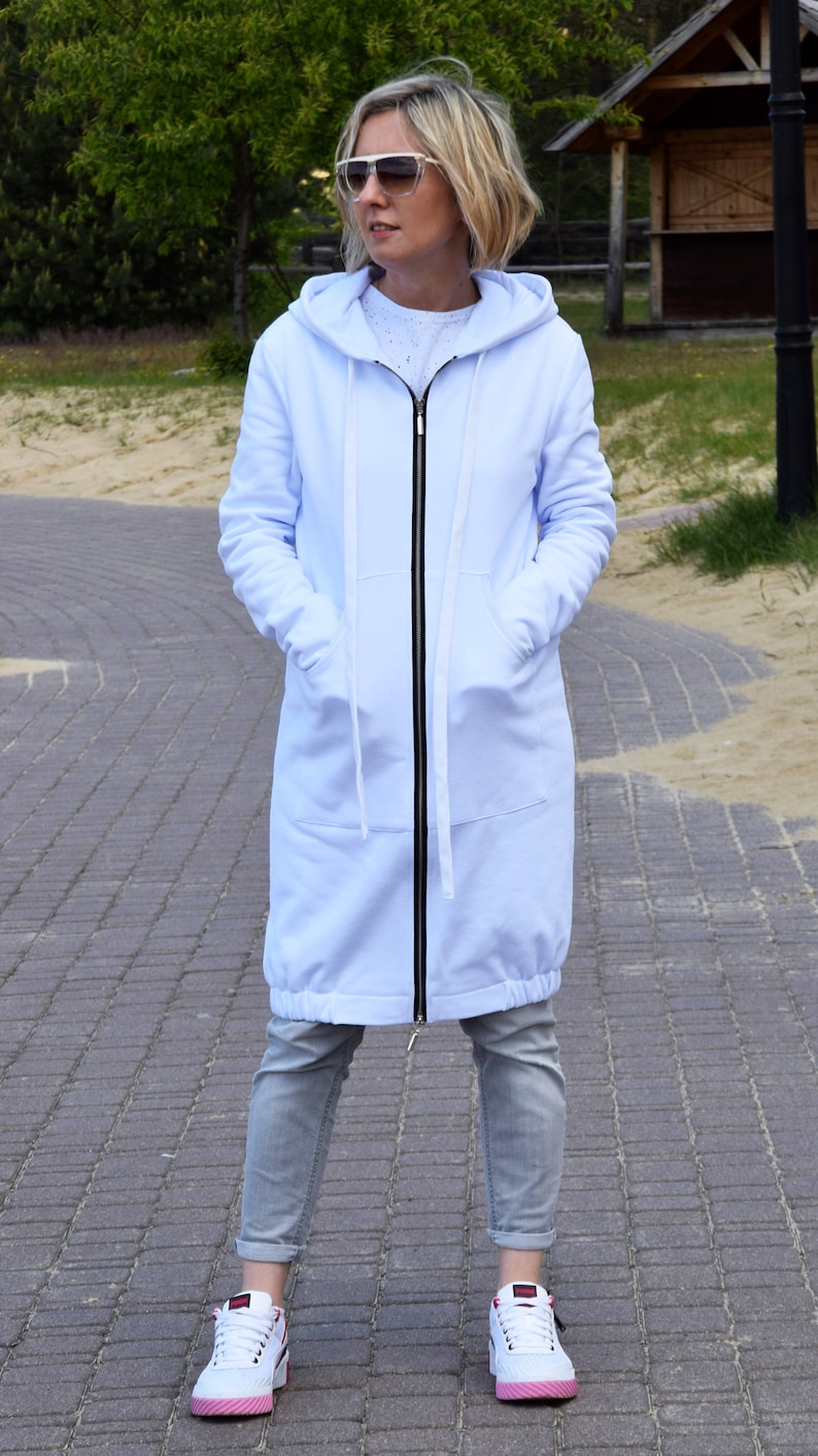 May include: A long, light blue hooded sweatshirt with a zipper closure. The sweatshirt has a relaxed fit and a drawstring hood. The model is wearing the sweatshirt with grey jeans and white sneakers.