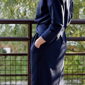 May include: A navy blue knee-length dress with long sleeves, a boat neckline, and a cinched waist featuring a tie belt. The garment includes side pockets and is constructed from a smooth, solid-colored fabric with a structured silhouette.