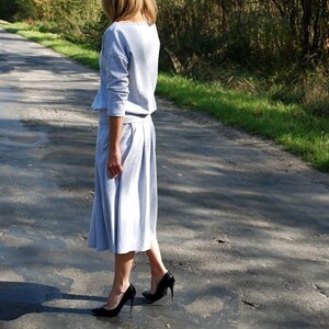 Puede incluir: Una mujer con un vestido de su&eacute;ter gris claro y tacones altos negros camina por un camino pavimentado.