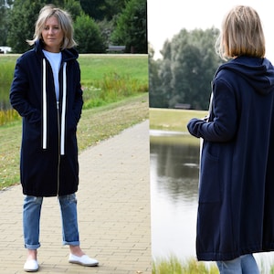 May include: A navy blue hooded sweatshirt with a zipper closure and white drawstrings. The sweatshirt has a long, relaxed fit and is shown being worn by a person in a park setting.