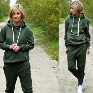 Pu&ograve; includere: Una felpa con cappuccio verde e pantaloni della tuta abbinati con lacci bianchi. La modella indossa l'outfit e scarpe da ginnastica bianche.