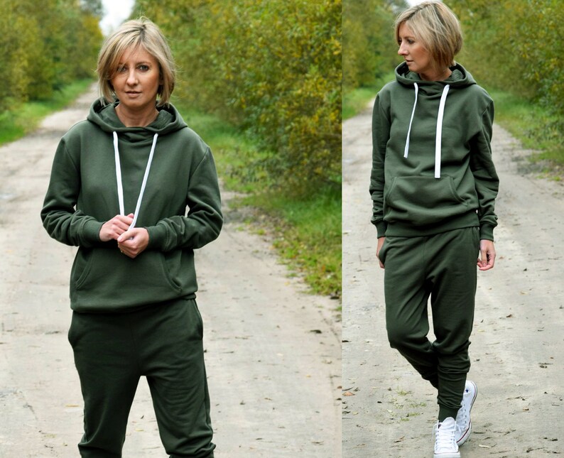 Pu&ograve; includere: Una felpa con cappuccio verde e pantaloni della tuta abbinati con lacci bianchi. La modella indossa l'outfit e scarpe da ginnastica bianche.