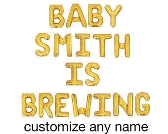 May include: Gold foil letter balloons spelling out the phrase BABY SMITH IS BREWING, arranged in four rows. Below the balloons, the black text reads customize any name. These metallic balloons are designed for party decoration and event signage.