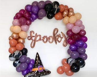 May include: A wreath of purple, pink, and orange balloons with a gold "Spooky" banner and a black witch hat.