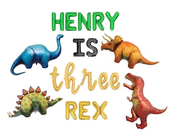 May include: A set of foil balloons featuring the text HENRY IS three REX in green, black, and gold. The display includes four dinosaur-shaped balloons: a blue long-necked dinosaur, an orange triceratops, a green stegosaurus, and a red tyrannosaurus.
