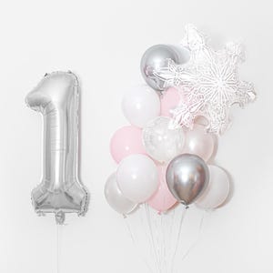 Könnte beinhalten: Ein großer silberner Folienballon in Form der Zahl Eins neben einem Bündel runder Luftballons in Weiß, Hellrosa und Metallic-Silber, gekrönt von einem großen weißen und silbernen schneeflockenförmigen Folienballon vor weißem Hintergrund.