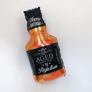 May include: A black and gold foil balloon shaped like a bottle of liquor with the text "Happy Birthday" and "Aged to Perfection" printed on it.