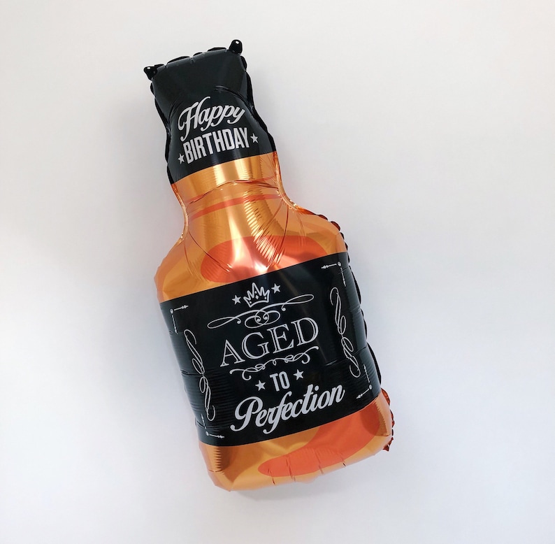 May include: A black and gold foil balloon shaped like a bottle of liquor with the text "Happy Birthday" and "Aged to Perfection" printed on it.