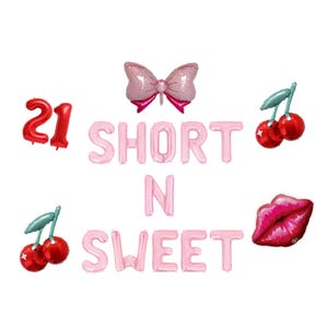 May include: Pink foil balloons spelling "SHORT N SWEET" with a red "21" balloon, a pink bow, red cherries, and a red lip-shaped balloon. Party decorations for a birthday or celebration.
