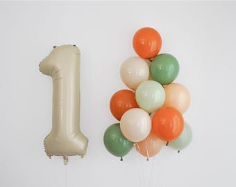 Op de afbeelding: Een beige cijfer één folieballon en een tros kleurrijke ballonnen. De kleuren van de ballonnen zijn oranje, wit, groen en perzik. De ballonnen zijn waarschijnlijk voor een verjaardag of viering.