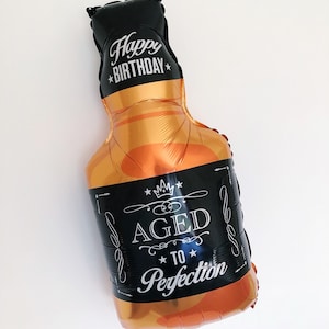 May include: A gold and black foil balloon shaped like a bottle of liquor with the text "Happy Birthday" and "Aged to Perfection" printed on it.