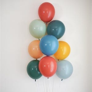 May include: A collection of ten colorful balloons in shades of red, green, blue, orange, and yellow, arranged in a triangular shape. Each balloon is tied with a white string, creating a festive and celebratory display.
