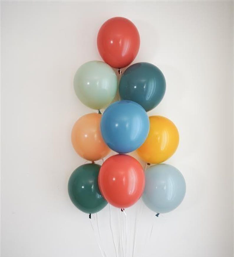 K&ouml;nnte beinhalten: Ein Arrangement aus zehn bunten Ballons in Rot-, Gr&uuml;n-, Blau-, Orange- und Gelbt&ouml;nen, angeordnet in einer dreieckigen Form. Jeder Ballon ist mit einer wei&szlig;en Schnur gebunden, was eine festliche Pr&auml;sentation ergibt.
