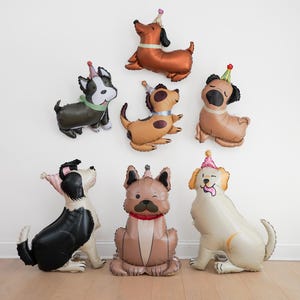 May include: A collection of dog-shaped balloons in various colors, each wearing a party hat. The balloons are arranged against a white wall and on a wooden floor, creating a festive and playful atmosphere, perfect for a birthday celebration.
