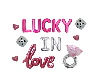 May include: Pink foil balloons spelling "LUCKY IN love" with heart and dice accents. A large pink diamond ring balloon is also included. Perfect for a romantic celebration or engagement party.