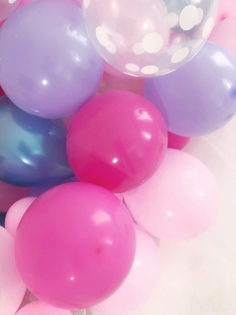 Pode incluir: Um grupo de bal&otilde;es inflados em v&aacute;rios tons de rosa, roxo e azul, incluindo um bal&atilde;o transparente com um padr&atilde;o de bolinhas brancas. Os bal&otilde;es est&atilde;o dispostos em um grupo denso, exibindo uma mistura de cores s&oacute;lidas e texturas transl&uacute;cidas.