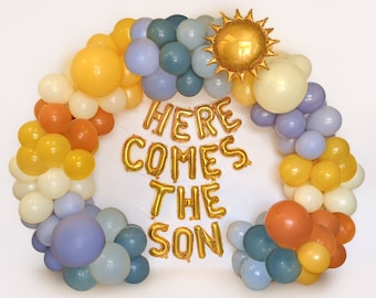 May include: A balloon arch in a rainbow of colors, including yellow, orange, blue, and white. The words "HERE COMES THE SON" are spelled out in gold foil balloons. A gold sun-shaped balloon is at the top.