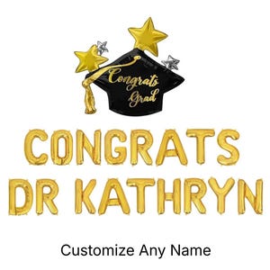May include: A black graduation cap balloon with gold stars and the text Congrats Grad, accompanied by gold letter balloons spelling CONGRATS DR KATHRYN. The display includes a gold tassel and the text Customize Any Name at the bottom.