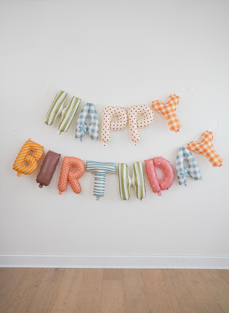 May include: A decorative banner spelling out HAPPY BIRTHDAY with individual fabric-covered letters. Each letter features a unique pattern, including stripes, polka dots, and gingham checks in various colors like orange, green, blue, and pink.