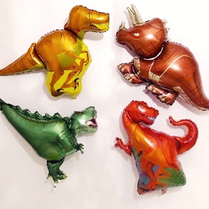 Puede incluir: Cuatro globos de aluminio con forma de dinosaurios. Un T-Rex amarillo y naranja, un triceratops marr&oacute;n, un T-Rex verde met&aacute;lico con la boca abierta y un T-Rex rojo y naranja con una cola curva y detalles de follaje verde.