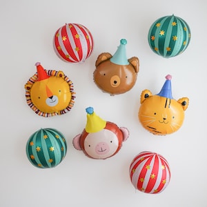Pu&ograve; includere: Una collezione di palloncini colorati a forma di animali e a righe. I palloncini includono un leone, un orso, una tigre e una scimmia, ognuno con un cappello da festa. I palloncini a righe sono rossi e bianchi o verde acqua e oro.