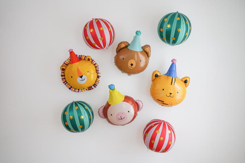 Pu&ograve; includere: Una collezione di palloncini colorati a forma di animali e a righe. I palloncini includono un leone, un orso, una tigre e una scimmia, ognuno con un cappello da festa. I palloncini a righe sono rossi e bianchi o verde acqua e oro.